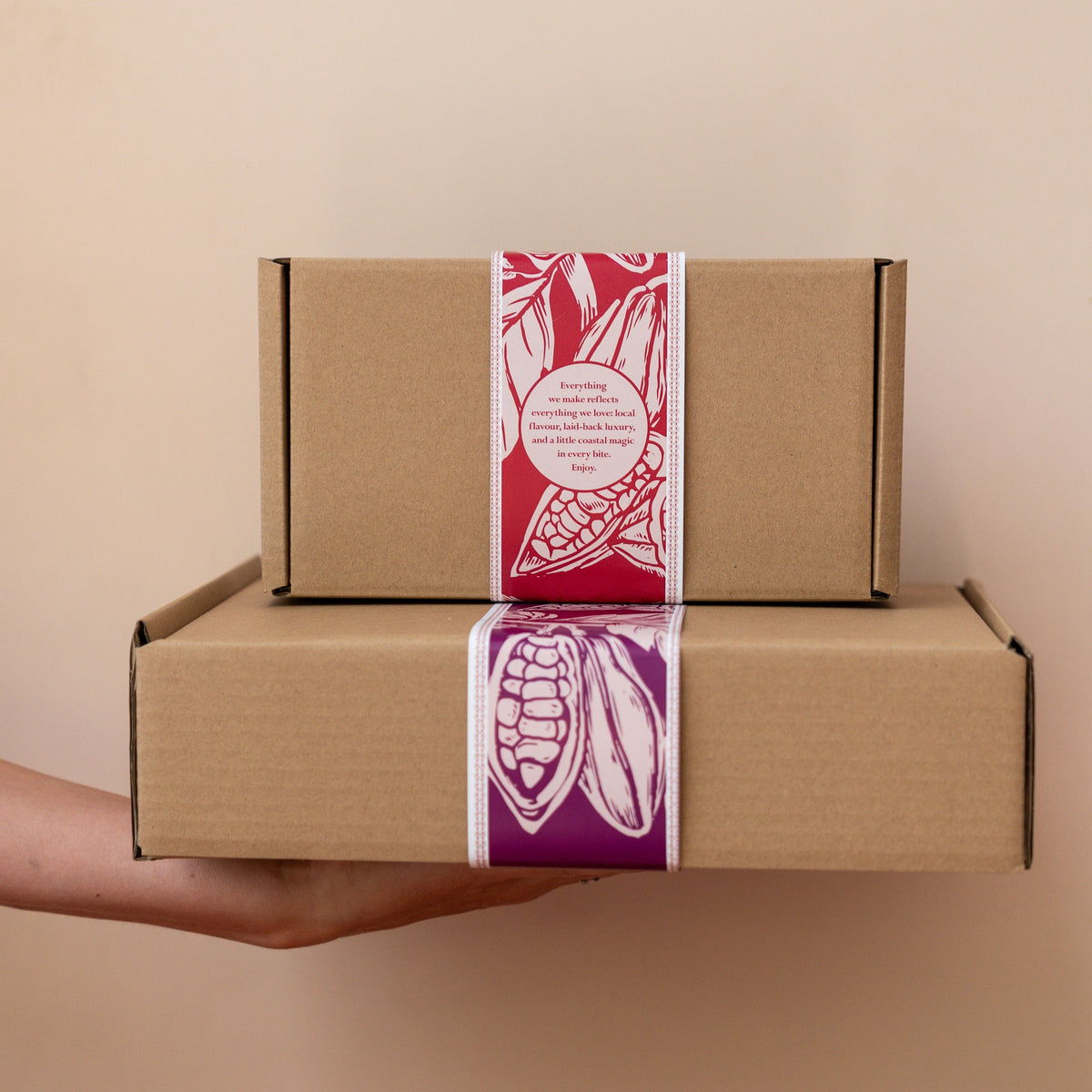 Two cardboard boxes with red and purple labels held against a beige background