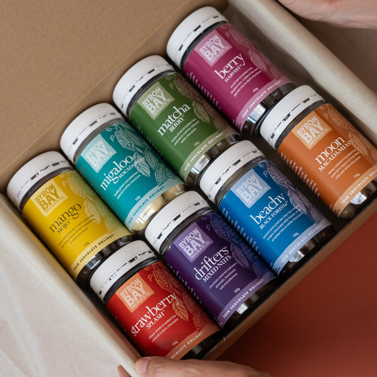 Assorted jars of baby food in a cardboard box held by hands.